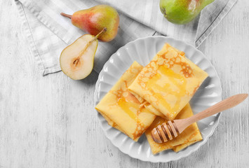 Delicious thin pancakes served with honey on plate against wooden background