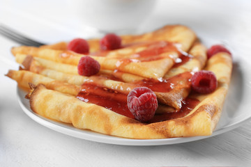 Delicious thin pancakes served with raspberries and jam on plate, closeup