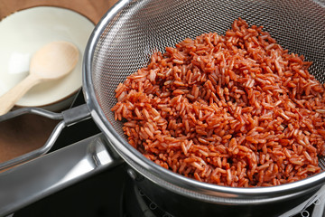 Sieve with brown rice in saucepan on stove