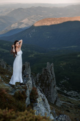 Perfect brunette beauty on a mountain. Woman in long red dress on the edge of a cliff in the mountains.