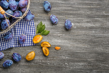 Basket with fresh ripe plums on wooden background