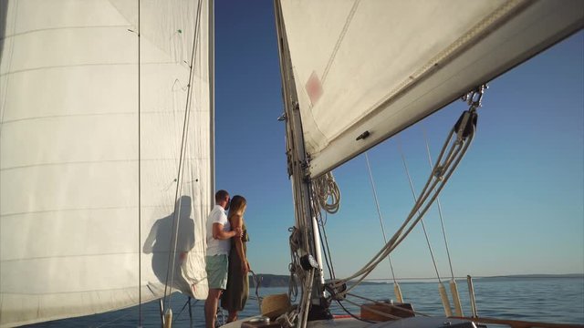 Happy couple is having a romantic evening sailing the river and watching sunset. Loving man is hugging his woman from the back and together they are enjoying the view.