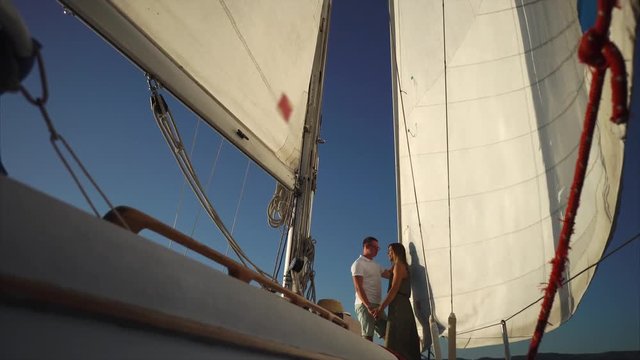 Low angle shot of yacht with loving couple standing under sail. Romantic sea trip