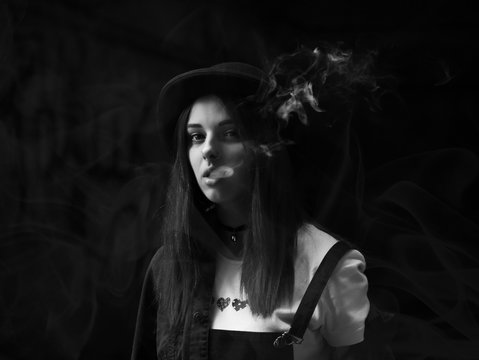 Emo girl smoking cigarette.Street punk or hipster woman with blue colorful dyed hair, hat, piercing,lenses,ears tunnels and unusual hairstyle stands in backyard. beautiful smoke.