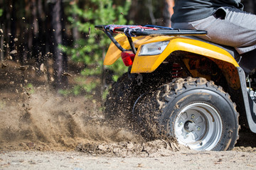 An ATV quadbike get stuck in a sandy road near forest and having wheel-spin making a spray of sand © Kirill Gorlov