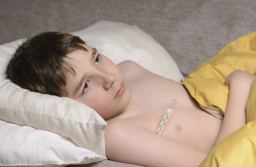 Niño con fiebre en la cama, tomandose la temperatura con el Termometro. 