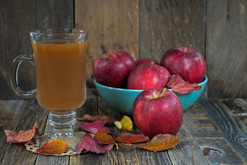 hot apple cider and red apples with autumn leaves on rustic barn wood