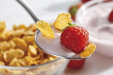 Strawberry yoghurt with cornflakes on a spoon