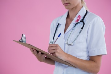 Mid section of female doctor writing on clipboard