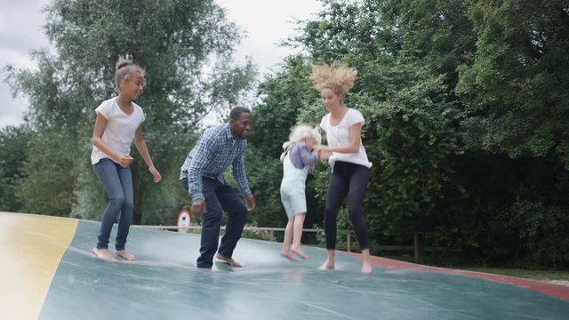  Happy mixed race family having fun, jumping on inflatable at activity centre