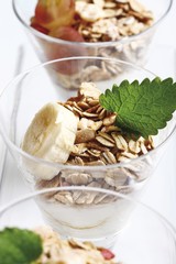 Muesli with yoghurt in a small glass jar, sliced banana, grapes, mint leafs