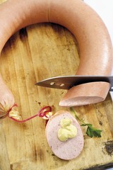 Ring of Pork Sausage on a wooden chopping block with mustard and a knife