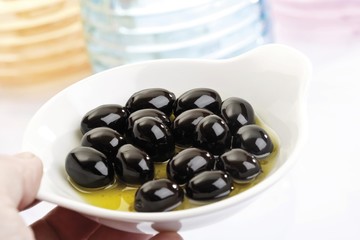 Hand holding black olives in small porcelain bowls