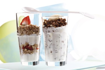 Muesli and chocolate muesli with yoghurt and in a small glass jar, sliced banana, strawberries, yoghurt spoon