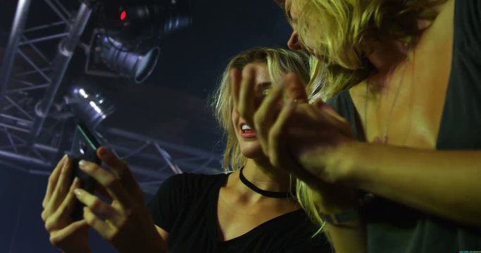 Female friends reviewing pictures on mobile phone at a concert 