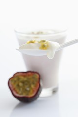 A glass of yogurt with a plastic spoon and a passionfruit