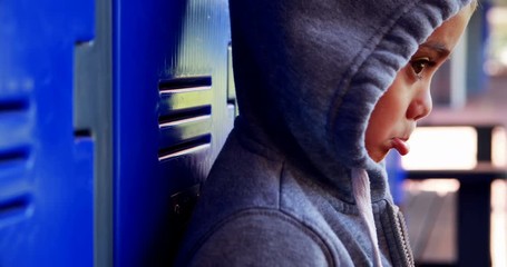 Sad schoolboy standing in locker room  - Powered by Adobe