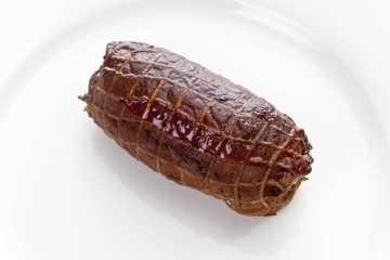 Braised pork roulade in a net on a porcelain plate