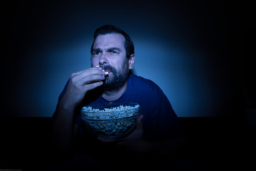 Man watching TV in disgust while eating popcorn