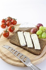 Camembert cheese on a board with grapes, bread and tomatoes