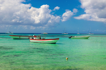 Naklejka na ściany i meble Wooden colorful boats on the azure clear water of the Caribbean Sea on a background of blue sky with white clouds, Dominican Republic