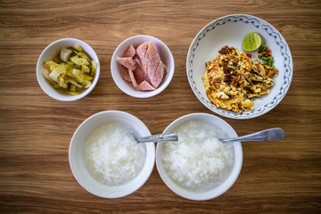 Thai food breakfast set, boiled rice, fried egg with lemon, sliced sour pork and pickled cabbage on wooden background