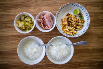 Thai food breakfast set, boiled rice, fried egg with lemon, sliced sour pork and pickled cabbage on wooden background