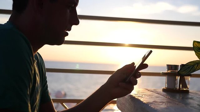 Young man in a cafe with a phone at sunset. HD, 1920x1080. slow motion
