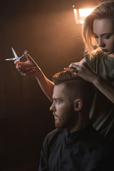 Female hairdresser cutting modern hipster hair. Hairdressing salon in dark place, stylish young...