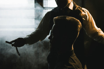 Stylish male shaving with dangerous sharp razor. Modern man style closeup, dark atmospheric...