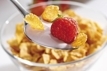 Strawberry yoghurt with cornflakes on a spoon