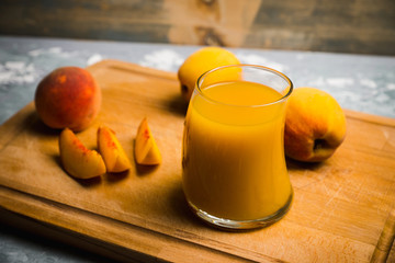 Glass of peach juice with fresh peaches on the rustic background. Shallow depth of field.