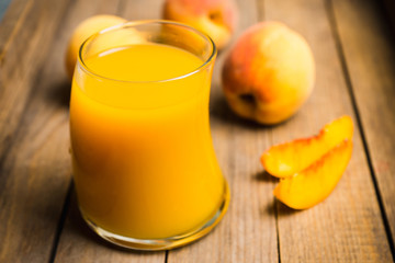 Glass of peach juice with fresh peaches on the rustic background. Shallow depth of field.