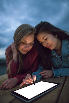Young artists draw on an empty graphic tablet, lying against a stormy evening sky with free space. Freelancers or art students draw digital pictures, look for inspiration, rest at night in the company