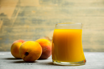 Glass of peach juice with fresh peaches on the rustic background. Shallow depth of field.