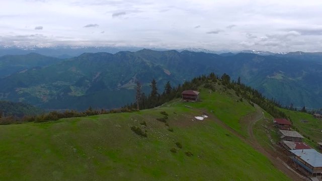 Flight over a green mountain range next to an abandoned village of shepherds, mountain valley covered coniferous woods at cloudy day after storm. Epic travel in mountains.