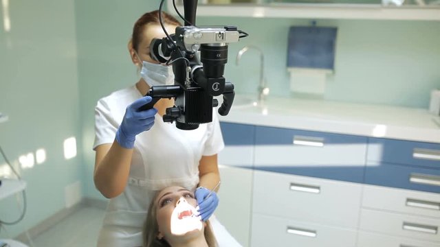 Dentist using dental microscope in dentistry for operation of a woman patient