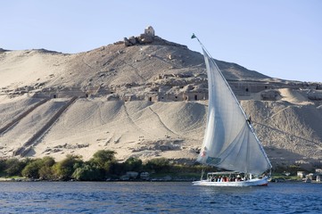 Felucca on the Nile River in front of the Qubbet el Hawa on the rock mountain and rock cut tombs and the grave of a sheikh on the summit, Aswan, Egypt, Africa