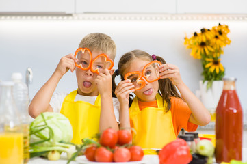 Happy kids having fun with food vegetables at kitchen holds pepper before his eyes like in glasses