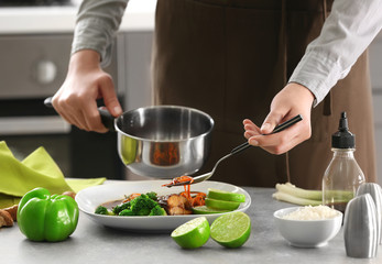 Chef putting carrot in sauce onto plate with fish in restaurant