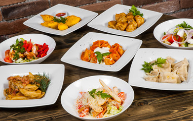Set of different salads, dumplings and ravioli on a wooden table