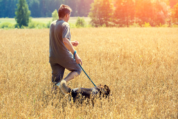 Man with dog on a leash running in an oat field in summer