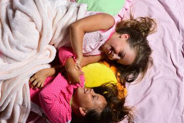 Schoolgirls in pink pajamas wallow on colorful pillows, top view