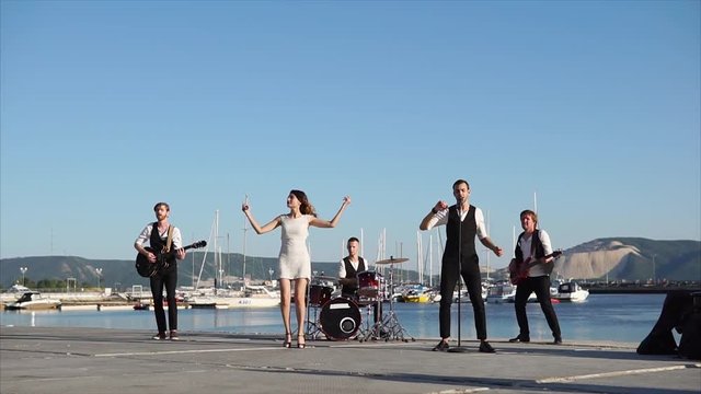 Slow motion shot of music band performing on waterfront in the harbour. Two leading singers, two guitarists and drummer