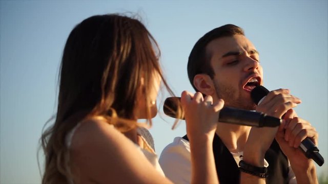 Slow motion shot of young man and woman singing a duet during outdoor musical festival