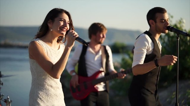Music band with man and woman duet singing a song and dancing. Outdoor concert on waterfront