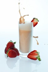 Strawberries falling into a drinking yoghurt or strawberry shake in a glass