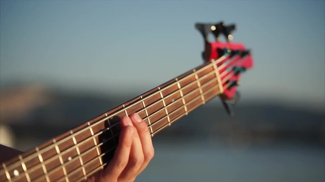 Close-up shot of a man playing bass guitar. View to the hand on fingerboard
