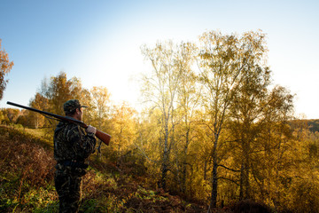 A hunter with a gun in the forest at dawn.
