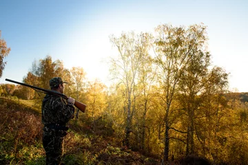 Foto op Plexiglas Jacht Een jager met een pistool in het bos bij dageraad.